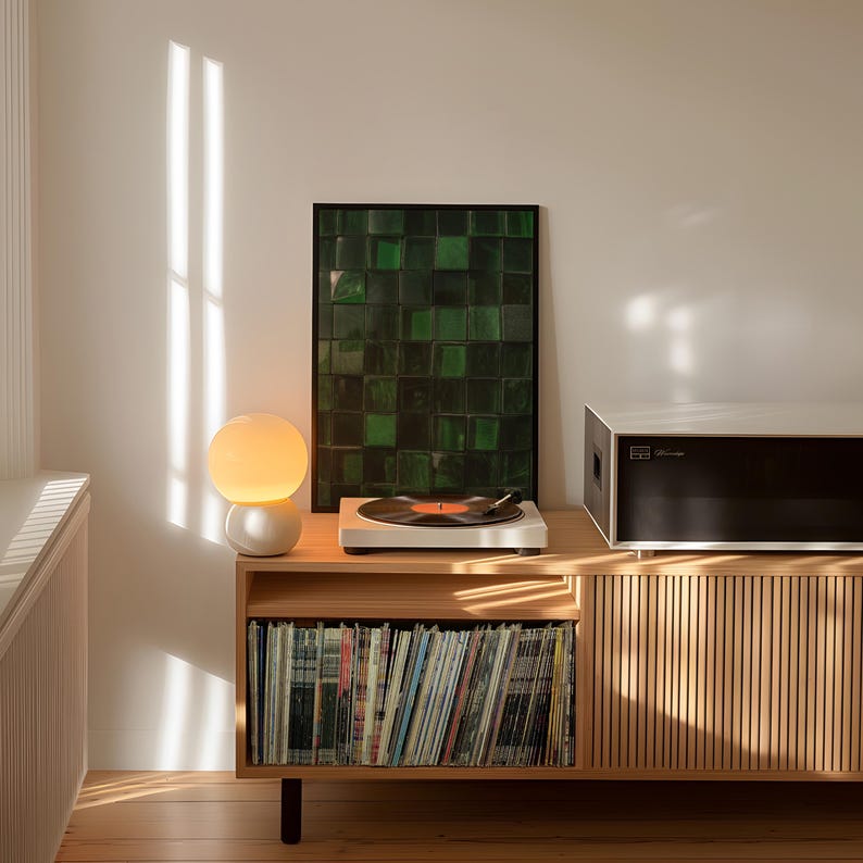 May include: A wooden media console with a record player, a framed green artwork, and a spherical lamp. The console has a section for vinyl records and a black and white stereo component. The room is lit by natural light.