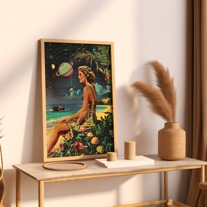 May include: A framed print of a woman sitting on a tropical beach with a large planet in the sky. The woman is wearing a gold dress and has long brown hair. The beach is surrounded by lush green foliage.