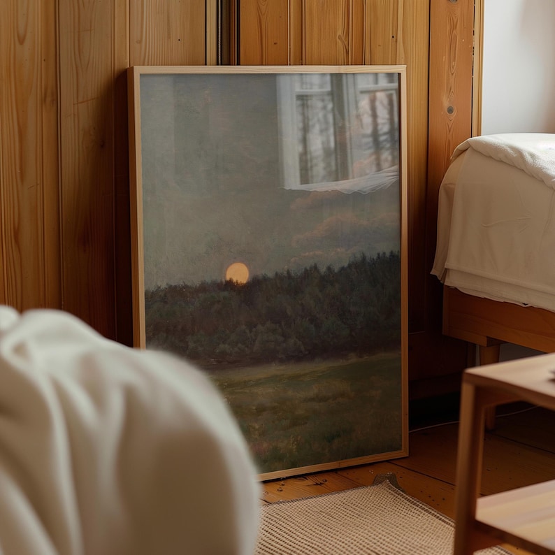 Puede incluir: Una impresi&oacute;n art&iacute;stica enmarcada que representa una puesta de sol sobre un bosque y un campo. La obra de arte est&aacute; en un marco de madera y se apoya en una pared de madera. La paleta de colores incluye verdes, amarillos y marrones.