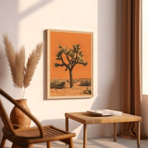 May include: A framed print of a Joshua tree in a desert landscape. The tree is silhouetted against a bright orange sky. The print is in a wooden frame.