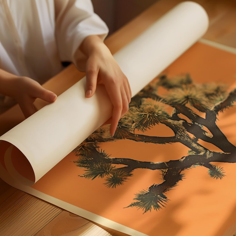 May include: A person unrolling a poster with a black and white illustration of a Joshua tree on an orange background.