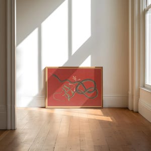 May include: A framed print of a black snake coiled around a vine with pink flowers on a red background.
