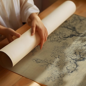 Puede incluir: Un rollo de papel blanco roto se desenrolla para revelar un dise&ntilde;o floral detallado en azul oscuro y beige. El rollo est&aacute; sobre una mesa de madera. La imagen muestra un primer plano del rollo y el dise&ntilde;o floral.