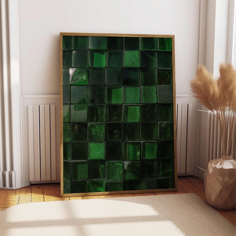 May include: A framed artwork featuring a mosaic of dark green, square tiles. The tiles have a glossy finish and are arranged in a grid pattern. The frame is a light brown color. The artwork is leaning against a white wall.