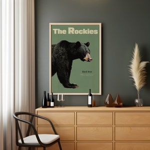 Pode incluir: Um p&ocirc;ster de estilo vintage com fundo verde que apresenta um urso preto com o texto "The Rockies" e "black bear" em uma moldura marrom.