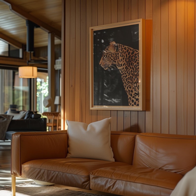 May include: A brown leather sofa with two white throw pillows in front of a wood-paneled wall. A framed print of a leopard is hanging on the wall above the sofa.