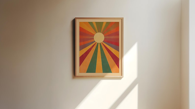 Op de afbeelding: Een ingelijste print van een kleurrijk zonnestralenontwerp met een witte cirkel in het midden. De achtergrond is lichtgeel met tinten rood, oranje, geel, groen en paars die vanuit het midden uitstralen.