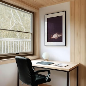 May include: A black office chair with a desk and a framed photograph of a surfer riding a wave. The desk has a laptop, a book, and a white lamp.