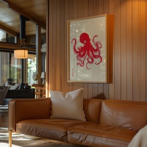 May include: A framed print featuring a red octopus illustration against a cream background. The artwork is displayed on a wooden wall above a brown leather sofa with a white pillow. The room has wooden paneling and a modern design.