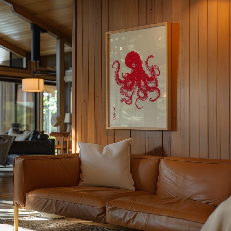 May include: A framed print featuring a red octopus illustration against a cream background. The artwork is displayed on a wooden wall above a brown leather sofa with a white pillow. The room has wooden paneling and a modern design.