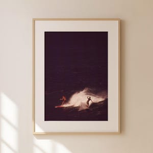 May include: Two people surfing on a wave in the ocean. The water is dark blue and the sky is a deep purple. The surfers are silhouetted against the sky.