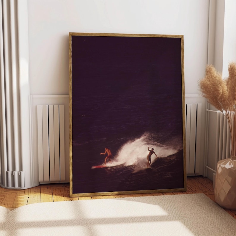 May include: A framed photograph of two people surfing on a wave. The photo is in a dark purple hue, with the wave breaking in the foreground. The surfers are silhouetted against the water.
