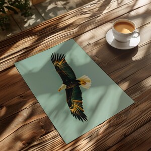 Pu&ograve; includere: Una stampa di un'aquila calva in volo, con le ali spiegate, su uno sfondo azzurro. Le piume dell'aquila sono dettagliate con sfumature di marrone, verde, giallo e bianco. Una tazza di caff&egrave; &egrave; su un piattino bianco su un tavolo di legno.