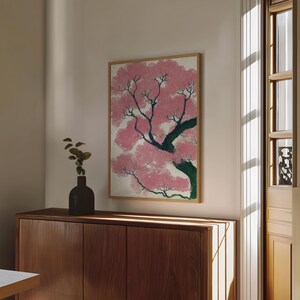 May include: A framed print of a cherry blossom tree in full bloom. The artwork features pink blossoms, dark green branches, and a light background. The print is displayed above a wooden cabinet.
