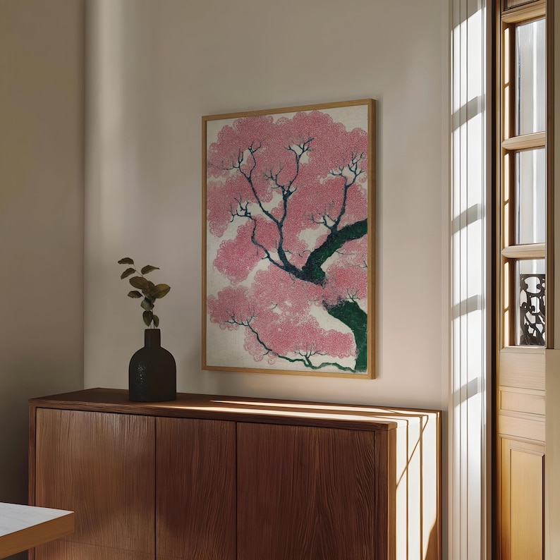 May include: A framed print of a cherry blossom tree in full bloom. The artwork features pink blossoms, dark green branches, and a light background. The print is displayed above a wooden cabinet.