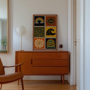 May include: A mid-century modern wooden cabinet with three drawers and a door. Above the cabinet, a framed artwork displays six colorful square designs, including a rainbow, sun, and wave. A gold lamp with a white globe shade sits on the cabinet.
