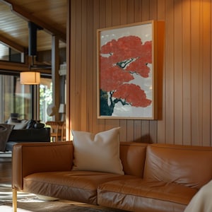 May include: A framed artwork featuring a stylized red tree with green and black accents hangs on a wood-paneled wall. A tan leather sofa with a white pillow sits below the artwork, creating a warm and inviting living space.