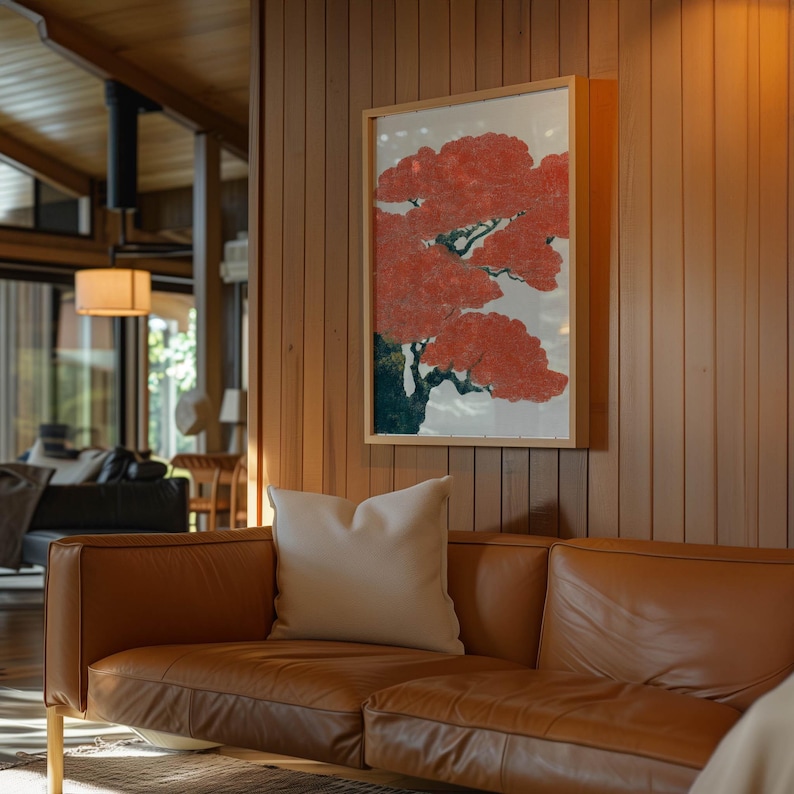 May include: A framed artwork featuring a stylized red tree with green and black accents hangs on a wood-paneled wall. A tan leather sofa with a white pillow sits below the artwork, creating a warm and inviting living space.