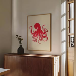May include: A framed print featuring a red octopus illustration on a cream background. The artwork is in a wooden frame and hangs above a wooden cabinet. The octopus design has a Japanese aesthetic.