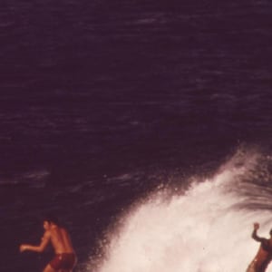 May include: Two people surfing on a wave. The wave is breaking and the water is white and foamy. The sky is dark blue.