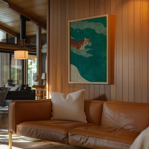 May include: A framed art print featuring a tiger swimming in a teal-colored sea with white clouds. The artwork is in a wooden frame and hangs on a wood-paneled wall above a brown leather sofa with a white pillow.