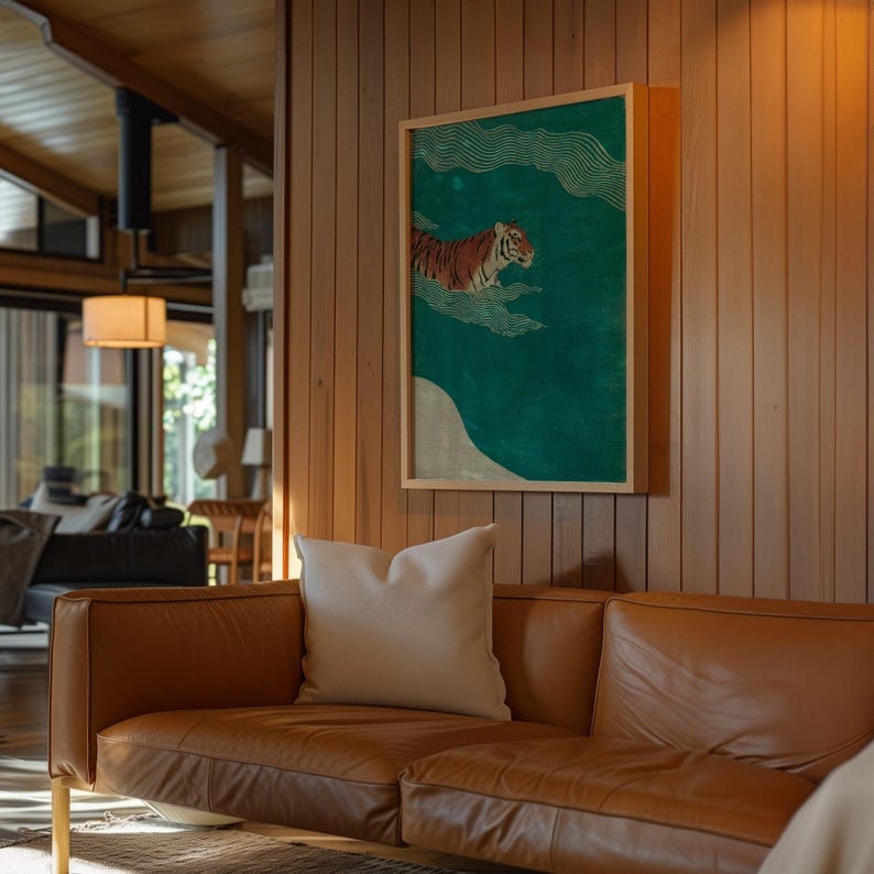 May include: A framed art print featuring a tiger swimming in a teal-colored sea with white clouds. The artwork is in a wooden frame and hangs on a wood-paneled wall above a brown leather sofa with a white pillow.