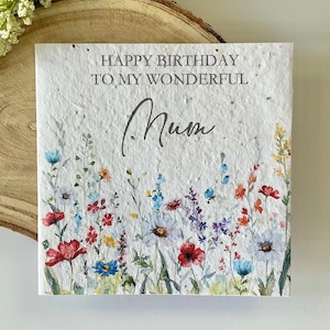 May include: A square greeting card made of textured white paper with embedded flecks. The text reads HAPPY BIRTHDAY TO MY WONDERFUL Mum. Below the text is a colorful watercolor illustration of various wildflowers in shades of red, blue, and yellow.