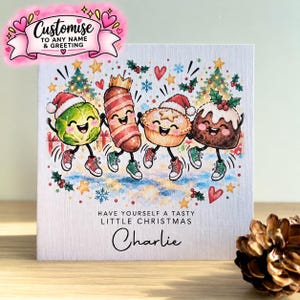 May include: A square greeting card featuring a cartoon illustration of a brussels sprout, a pig in a blanket, a mince pie, and a Christmas pudding, all wearing Santa hats and sneakers. Text reads: HAVE YOURSELF A TASTY LITTLE CHRISTMAS Charlie.