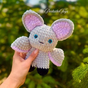 May include: A handmade gray crochet mouse toy with large ears lined in lavender. The mouse has blue embroidered eyes and black feet. The text "Peekabo Toys" is in the background.