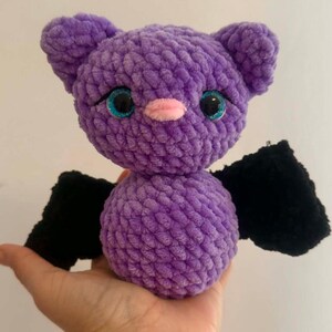 May include: A handmade purple crochet bat plush toy with black wings and sparkly blue eyes. The bat has a pink nose and small ears. The text "PeekaboToys" is in the upper right corner.