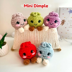 Può includere: Cinque personaggi Mini Dimple rotondi, in peluche lavorato all'uncinetto, nei colori beige, verde lime, viola, rosso e azzurro. Ognuno ha occhi di sicurezza neri, guance ricamate rosa, un piccolo sorriso e due piedini rotondi bianchi o marroni.