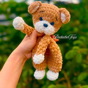May include: A handmade, plush teddy bear in shades of brown and white. The bear has a textured, fuzzy appearance with white accents on its paws, ears, and muzzle. The bear's eyes are blue, and the text "PeekaboToys" is visible.
