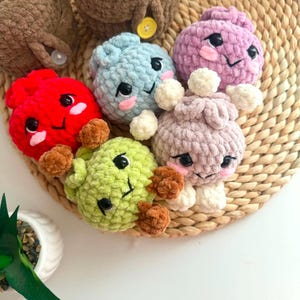 Puede incluir: Una colecci&oacute;n de seis peque&ntilde;as figuras de peluche tejidas a ganchillo con hilo suave y texturizado. Cada figura presenta ojos de pl&aacute;stico negro, sonrisas bordadas y mejillas rosadas. Los colores incluyen rojo, azul claro, morado, verde claro y beige.