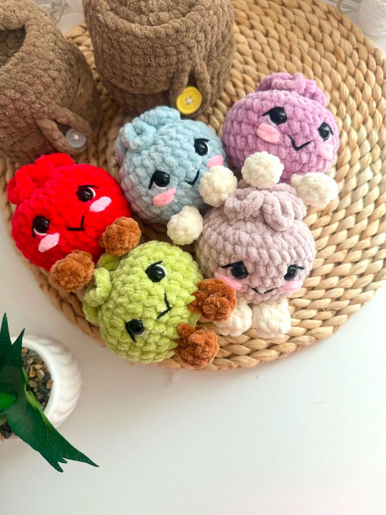Puede incluir: Una colecci&oacute;n de seis peque&ntilde;as figuras de peluche tejidas a ganchillo con hilo suave y texturizado. Cada figura presenta ojos de pl&aacute;stico negro, sonrisas bordadas y mejillas rosadas. Los colores incluyen rojo, azul claro, morado, verde claro y beige.