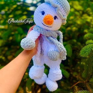 May include: A handmade crochet snowman doll with a white body, gray hat, scarf, and mittens. The snowman has a bright orange nose and black eyes. The doll is approximately 8 inches tall.