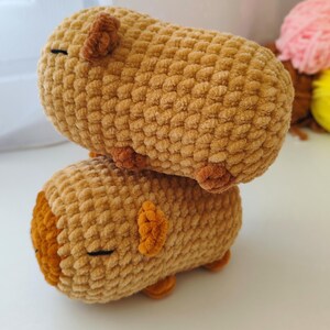 May include: Two brown crocheted plush toys shaped like guinea pigs. The toys are stacked on top of each other.