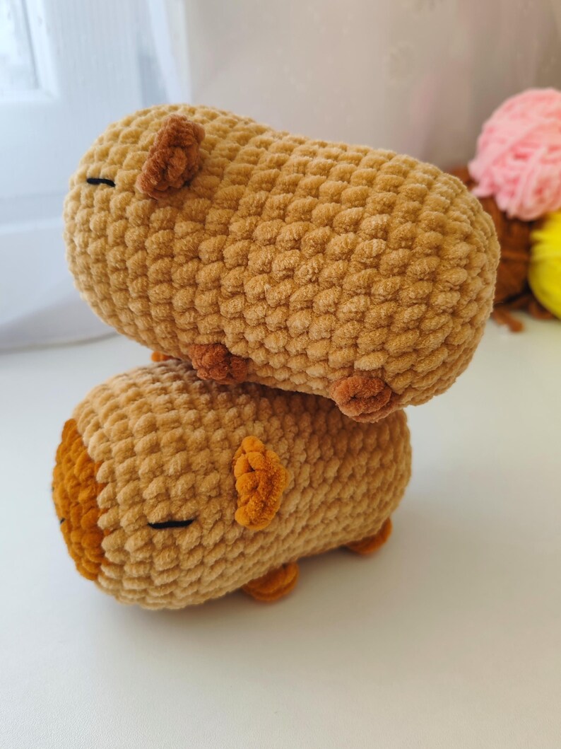 May include: Two brown crocheted plush toys shaped like guinea pigs. The toys are stacked on top of each other.