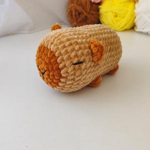 May include: A small, brown crocheted stuffed animal with a sleepy face. The animal is lying on its side with its head resting on its paws.