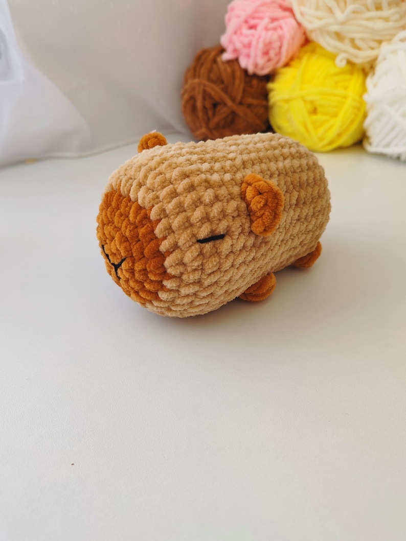 May include: A small, brown crocheted stuffed animal with a sleepy face. The animal is lying on its side with its head resting on its paws.