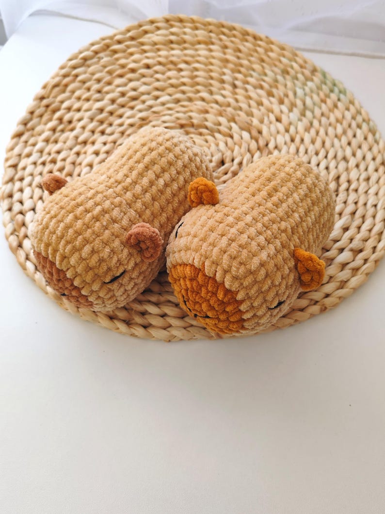 May include: Two crocheted brown and orange bear plushies with closed eyes, lying on a woven straw mat.