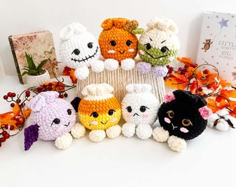 May include: A collection of seven small, round, crocheted plush figures with various facial expressions and colors, including white, orange, green, purple, yellow, and black. Each plush features small white feet and embroidered details.