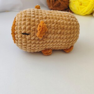 May include: A brown crocheted plush toy shaped like a pig. The toy has small orange ears and feet.