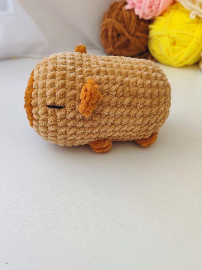 May include: A brown crocheted plush toy shaped like a pig. The toy has small orange ears and feet.