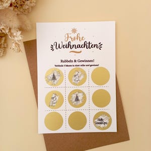 May include: A festive scratch card with the German phrase "Frohe Weihnachten" in gold lettering. The card has nine scratch-off panels, some showing Christmas tree and bunny designs. The text "Rubbeln & Gewinnen!" is also visible.