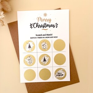 May include: A white Christmas scratch card with gold foil circles and the text "Merry Christmas". The card includes the text "Scratch and Match! MATCH 3 TREES IN A ROW AND WIN!" and "We're pregnant!" on a brown envelope.