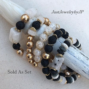 May include: A set of beaded bracelets featuring a variety of stones and textures. The bracelets include black lava beads, gold-colored metal beads, and clear and white stone beads. The text "JustJewelrybyJP" and "Sold As Set" are visible.