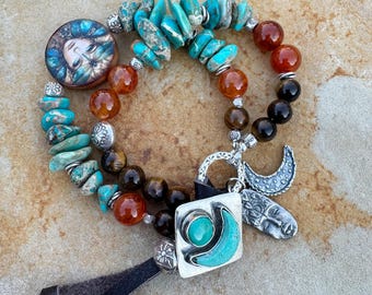May include: A collection of handcrafted bracelets featuring turquoise, carnelian, and tiger's eye beads. One bracelet has a round pendant with a painted face, while others have silver charms, including a crescent moon and a face.