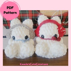 May include: Two crocheted bunny amigurumi toys, one with a white and gray color scheme and the other with a white and red color scheme. The toys are sitting on a red and white plaid surface. The text "PDF Pattern" is visible in the upper left corner of the image.