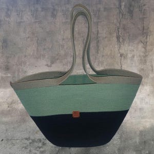 May include: A large, green and black tote bag made of rope. The bag has a wide, open top and two long handles. The bag is made of a thick, durable rope and has a natural, rustic look.
