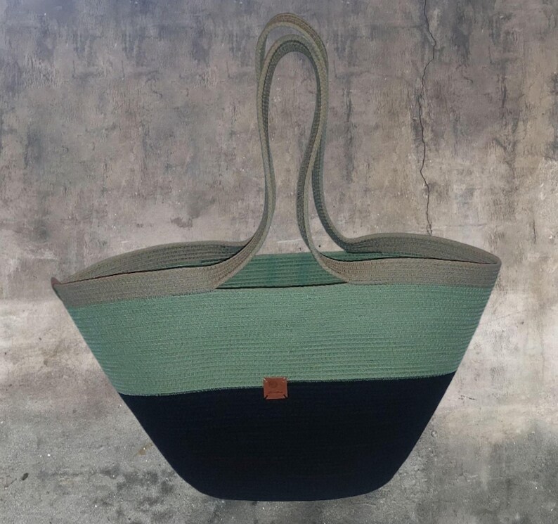 May include: A large, green and black tote bag made of rope. The bag has a wide, open top and two long handles. The bag is made of a thick, durable rope and has a natural, rustic look.